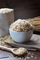 Hot Cook and raw brown rice in white ceramic bowl on wood table and wood background with spoon. Copy space.
