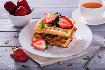 Plate of Belgian waffles with chocolate sauce and fresh  strawberries on white background. Delicious sweet dessert with cup of  tea.