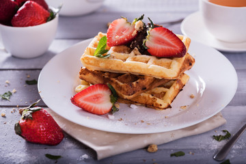 Plate of Belgian waffles with chocolate sauce and fresh  strawberries on white background. Delicious sweet dessert with cup of  tea.