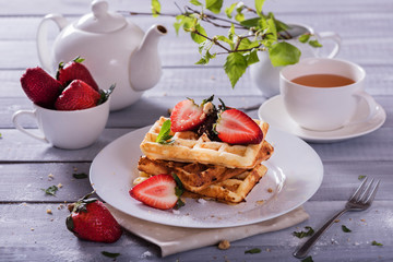 Plate of Belgian waffles with chocolate sauce and fresh  strawberries on white background. Delicious sweet dessert with cup of  tea.
