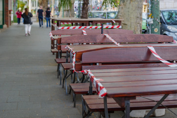 Red and white caution tape wrapped around outdoor tables and seats area of cafe which closed during global quarantine from COVID-19. Lockdown  and quarantine time in epidemic of COVID-19 Virus crisis.