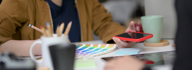 Cropped shot of female designer working with smartphone and designer supplies