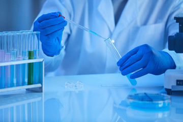 Close-up of scientist in protective gloves holding pipette and examining the analysis in test tube