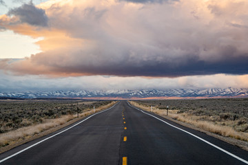 Road leading through the landscape towards snowy mountains and cloud