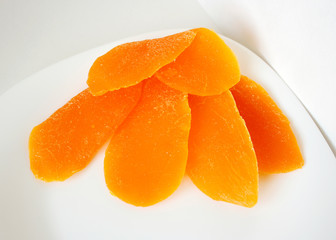 Dried crystallized mango on a plate on a white table. Photo close-up of dried mango pieces.