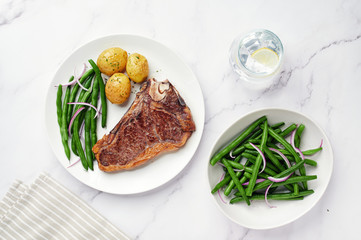 Dry Aged Beef Steak with potatoes and green beans.Dry aged  sirloin steak with green beans salad and glass of water on white marble table