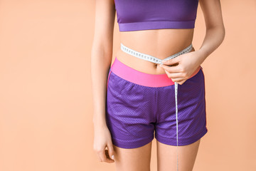 Young woman with measuring tape on color background. Weight loss concept