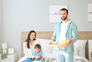 Obraz premium Happy man bringing his family breakfast in bed