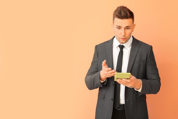 Confused young man with calculator on color background