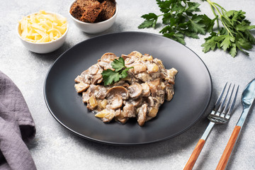 Stewed mushrooms champignons in sauce with sour cream and cheese parsley on a plate.