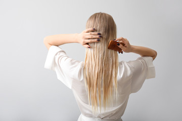 Young woman combing her hair against grey background