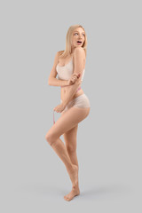 Slim woman with measuring tape on grey background. Weight loss concept