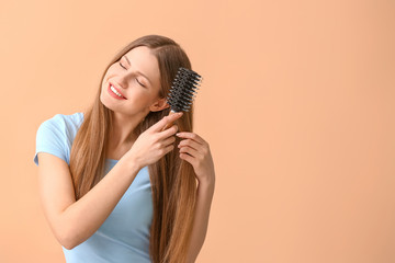Beautiful young woman brushing hair on color background