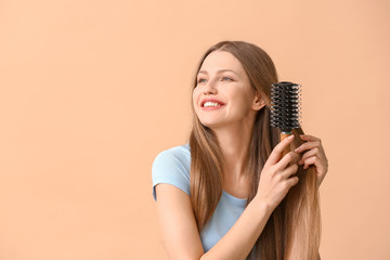 Beautiful young woman brushing hair on color background