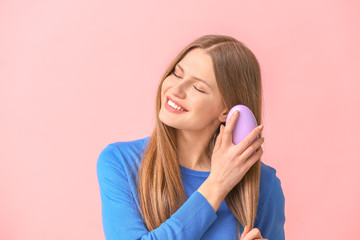 Beautiful young woman brushing hair on color background