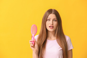 Surprised young woman with hair brush on color background