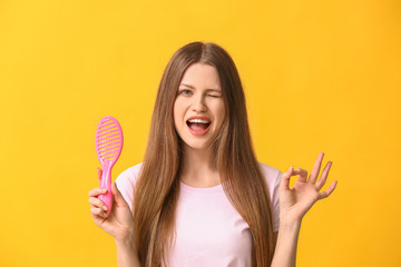 Beautiful young woman with hair brush showing OK on color background