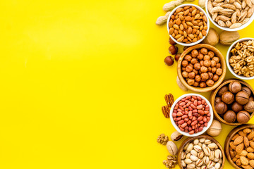 Set of macadamia, hazelnut, walnut, almond, pistachio, pecans nuts on yellow background top-down frame copy space