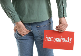 Young man holding paper with text HEMORRHOIDS on white background