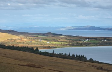 Panoramic view of the shores, mountains and valleys of Jura island from the water. Cloudy blue sky....