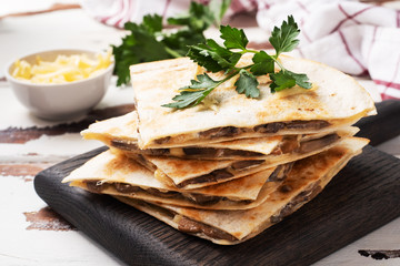 Pieces of quesadilla with mushrooms sour cream and cheese on a wooden stand with parsley leaves. Wooden background copy space.
