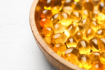 Bowl of fish oil capsules on white wooden background, closeup