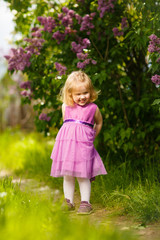 funny little girl near bush of lilac with bouquet 