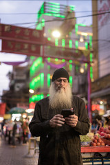 Mature bearded tourist man with eyeglasses using phone in Chinatown at night