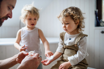 Father putting bandage on small hurt toddler child indoors at home.