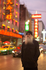 Mature bearded tourist man with sunglasses thinking in Chinatown at night