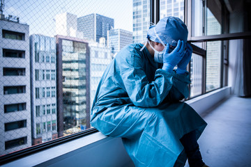 窓辺に座り込み顔を覆う医師