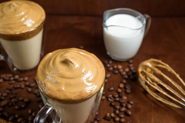 cold dalgona coffee in clear glasses on a dark wooden background. froth of sugar and instant coffee whipped with a mixer on top of cold milk. close up. Korean and Indian whipped coffee.