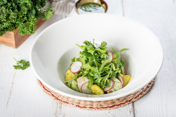 Salad with potatoes, radishes, fresh herbs in a white plate