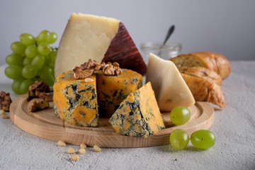 Pieces of Jugas and Shropshire Blue  cheese with grapes on a wooden plate at  background