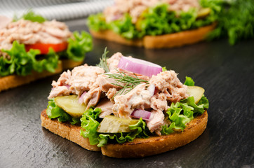 Tuna sandwiches with lettuce tomatoes pickles and onions on slate