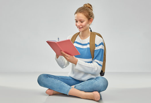 Education, Travel And Tourism Concept - Happy Smiling Teenage Student Girl With School Bag Or Backpack And Notebook Sitting On Floor Over Grey Background