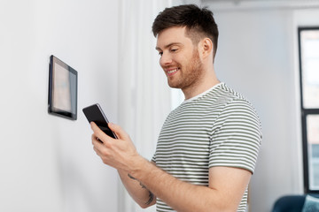 automation, internet of things and technology concept - happy smiling man with smartphone using tablet pc computer at smart home
