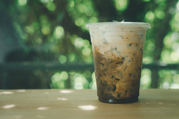 Ice coffee on a wood table with cream being poured into it showing the texture