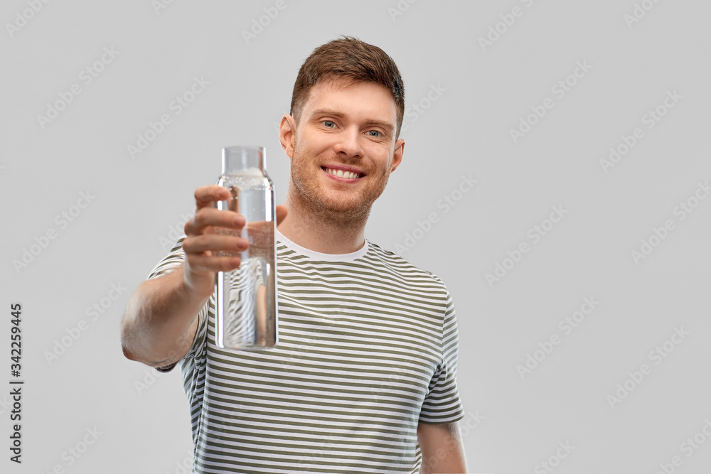 Wall mural sustainability, consumerism and eco friendly concept - happy smiling man holding water in reusable glass bottle grey background