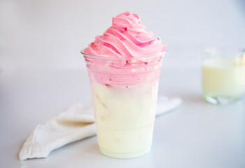 Home made Dalgona whipped strawberry in a cup on white table with a cup of milk background.