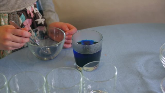Little girl makes paint closeup blue powder in water for eggs Easter holiday caucasian white child