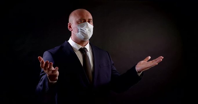 portrait of a man in a business suit on a black background. he wears a disposable mask, gestures with his hands, speaks, gives a thumbs-up and removes the masque