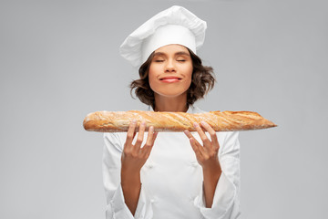 cooking, culinary and bakery concept - happy smiling female chef or baker in toque holding french bread or baguette over grey background