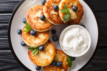 Hot traditional syrniki with blueberries, mint and sour cream closeup in a plate. Horizontal top view