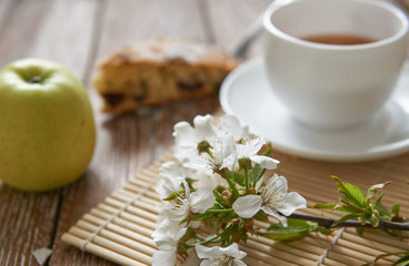 Homemade apple pie with cinnamon and cup of tea on wooden table.