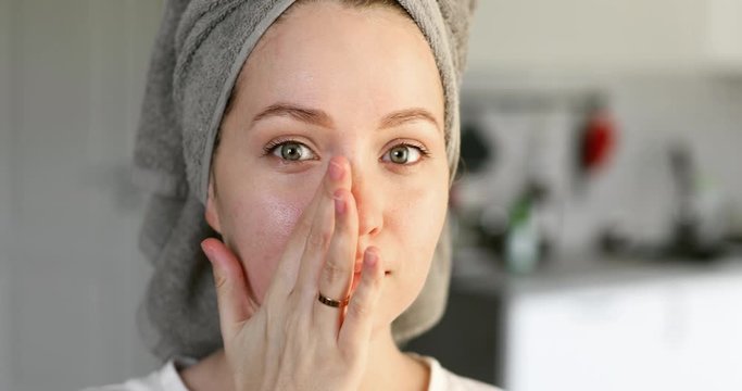 Portrait of woman is removing facial moisturising mask from face, front view. Young girl making treatment fo facial skin care. She looking at camera. Beauty treatment. Rejuvenation of skin.