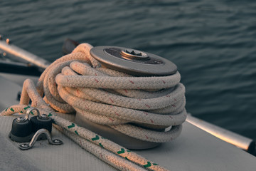 closeup white rope wrapped around sail boat winch at sunset. Yachting concept and sea background