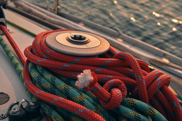 close up red and green rope wrapped around winch of sail boat at sunset. Yachting concept and sea...