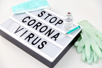 medicine, epidemic and healthcare concept - close up of lightbox with stop coronavirus caution words, protective mask, gloves and syringe with drug on white background