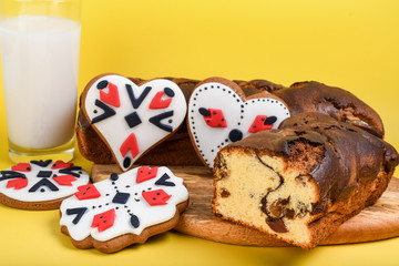Slices of Romanian sponge cake or chec, cozonac with red traditional towel with manual stitch on wooden board, Easter painted eggs and home made ginger bread hearts, Authentic Easter Brunch concept. 